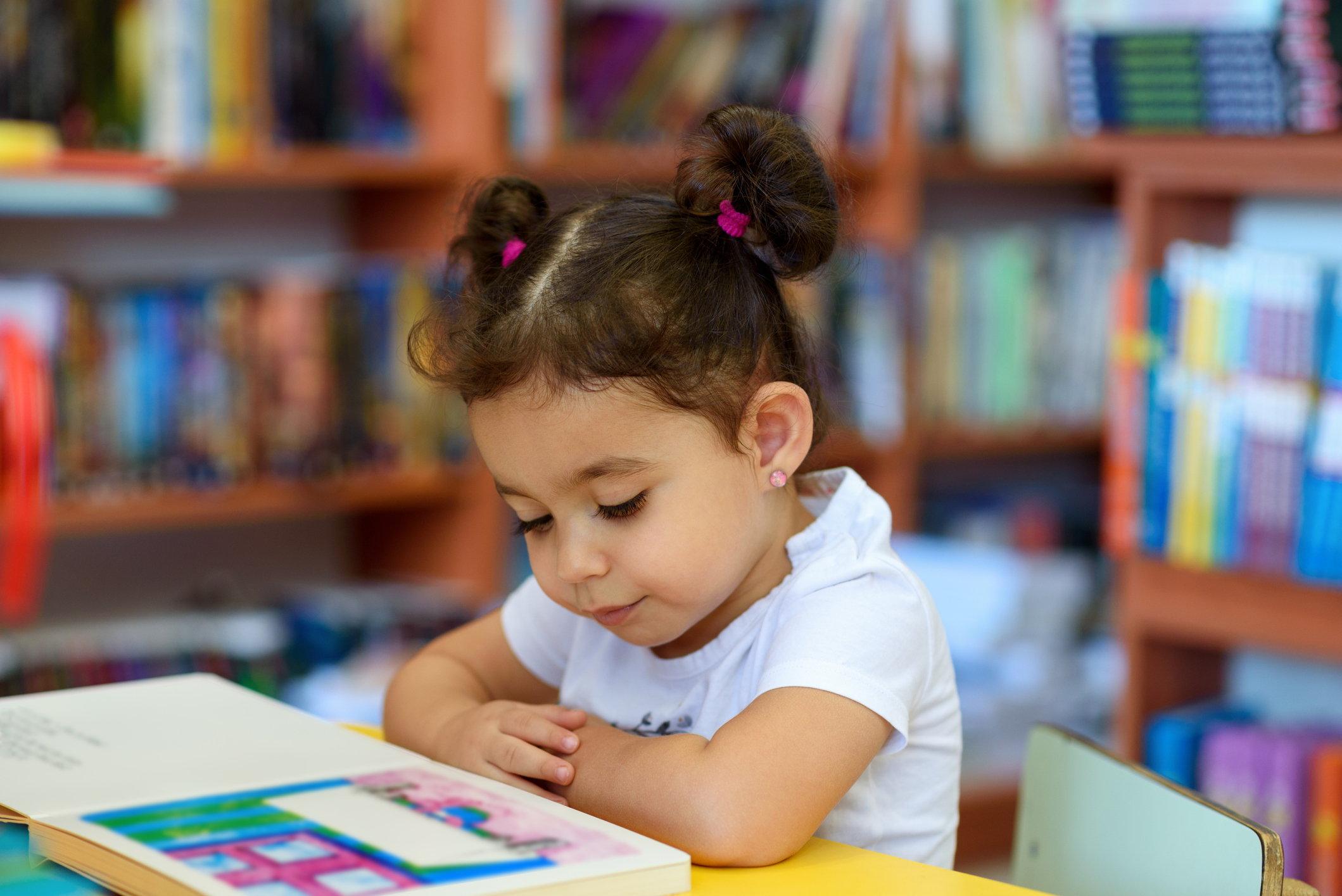 A little girl reading a book in a library.